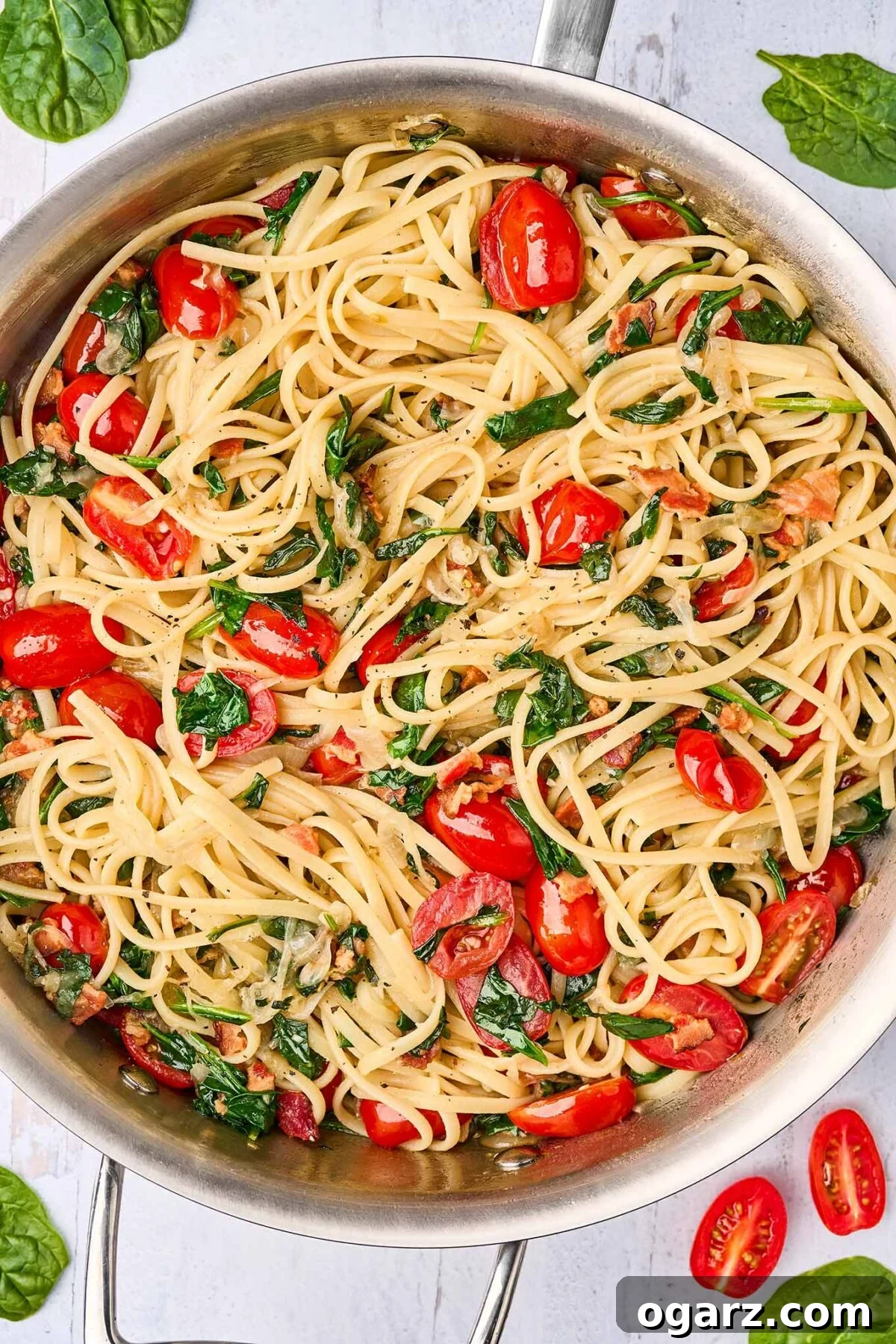 Decadent Blue Cheese Pasta with Crispy Bacon and Sweet Caramelized Onions 6 A large sauté pan containing cooked linguine pasta, perfectly tossed with a rich mixture of golden caramelized onions, crispy bacon pieces, vibrant fresh spinach, and halved grape tomatoes, awaiting the final addition of crumbled blue cheese.
