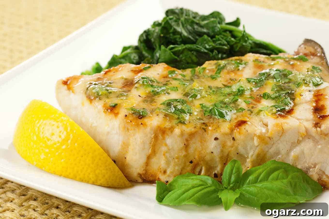 Bright Grilled Swordfish with Lemon-Basil Butter 3 A grilled swordfish steak with melted butter and chopped basil, garnished with a lemon wedge and sprig of basil, sautéed spinach in the background.