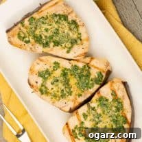 A serving plate with three portions of grilled swordfish steaks topped with lemon basil butter, a grilling fork to the left and napkin beneath the plate.