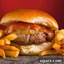 A close view of a grilled burger topped with cheddar cheese, maple ketchup and grilled onions on a slate board, fries to the side.