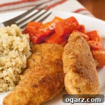 Two spicy breaded chicken tenderloins on a plate with glazed carrots and quinoa, a fork and kitchen towel in the background.