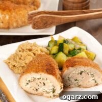 Rolled, crumb-coated chicken breasts filled with herbed goat cheese, served with sautéed zucchini and orzo on a square white plate, more chicken in the background.
