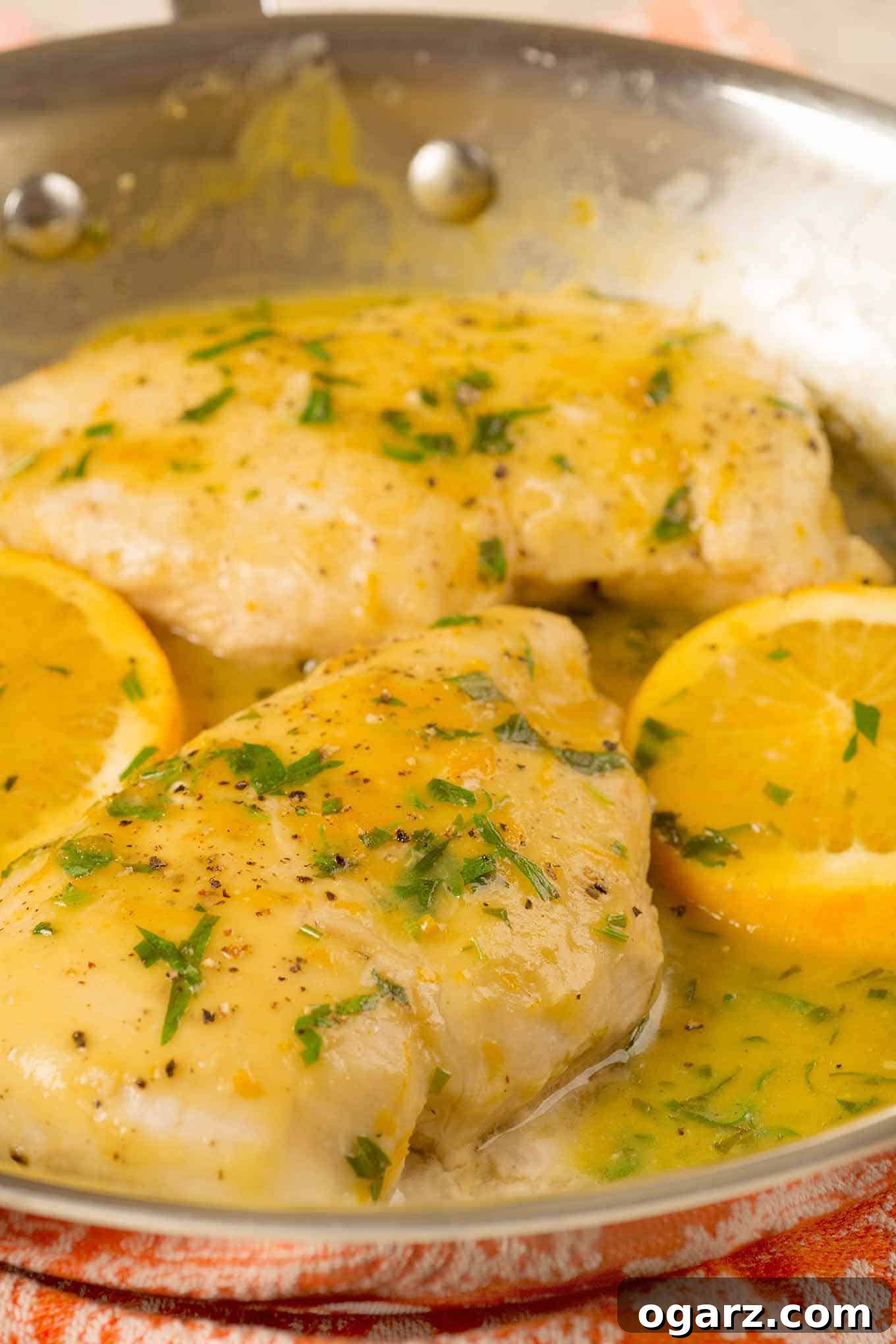 Zesty Orange Tarragon Chicken 3 Close-up view of succulent boneless chicken breasts simmering in a rich orange and fresh tarragon pan sauce, adorned with vibrant orange slices, all in a single skillet, showcasing the delicious details.