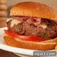 Juicy Tuscan-style burger topped with melted cheese and prosciutto, served on a soft bun with tomato slice and a side of seasoned potato wedges.