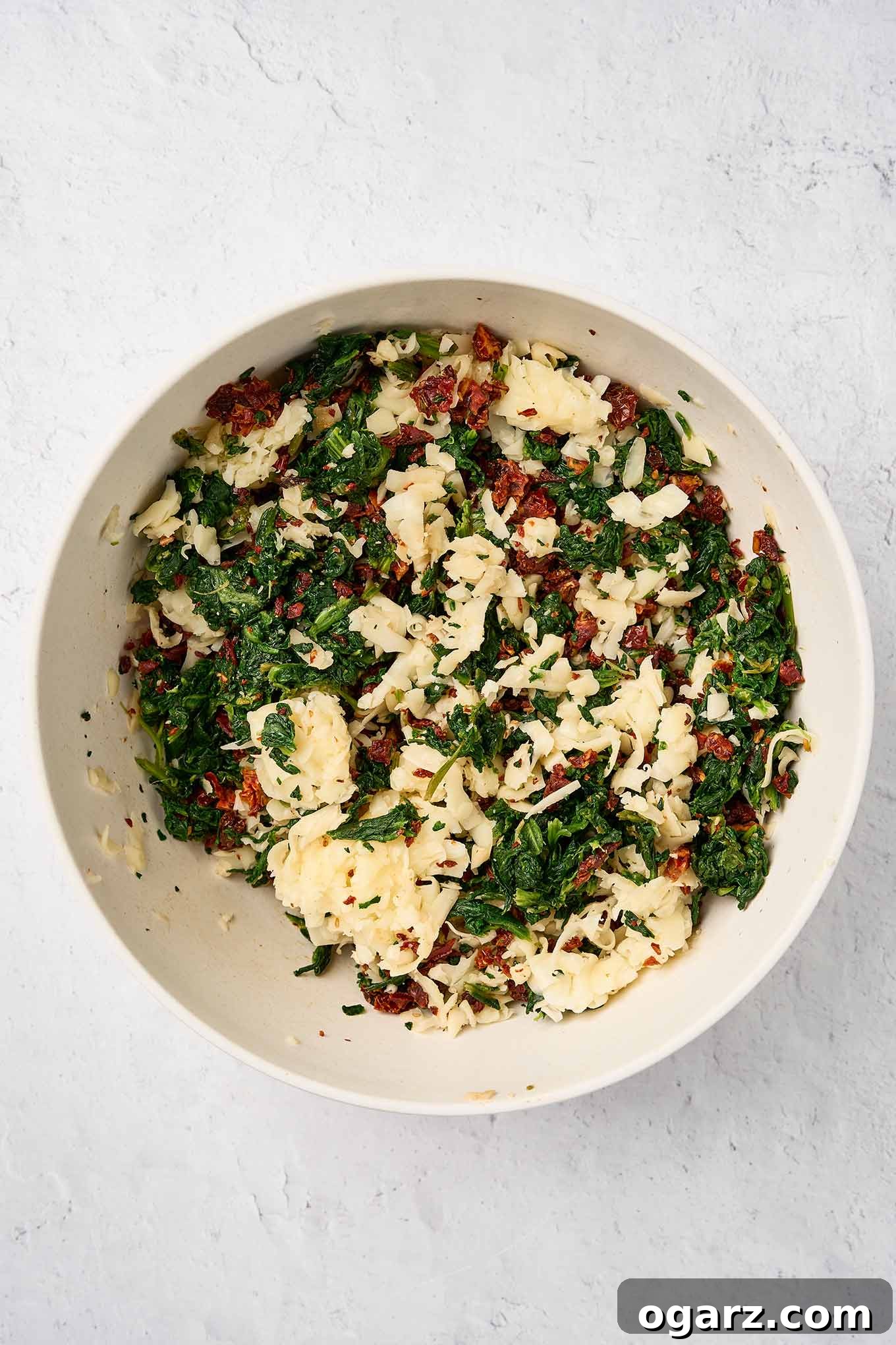 Savory Spinach Swirls 4 Spinach pinwheel filling mixture in a bowl ready for mixing; chopped spinach, sun-dried tomatoes, and grated fontina.