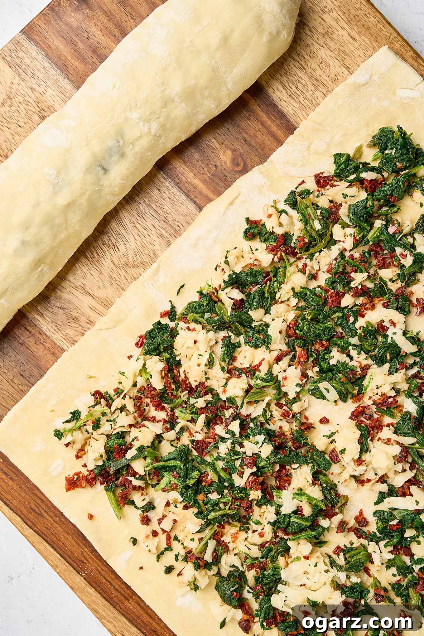 Savory Spinach Swirls 5 Puff pastry sheet topped with spinach, sun-dried tomatoes, and cheese filling, shown next to an already rolled pastry log.