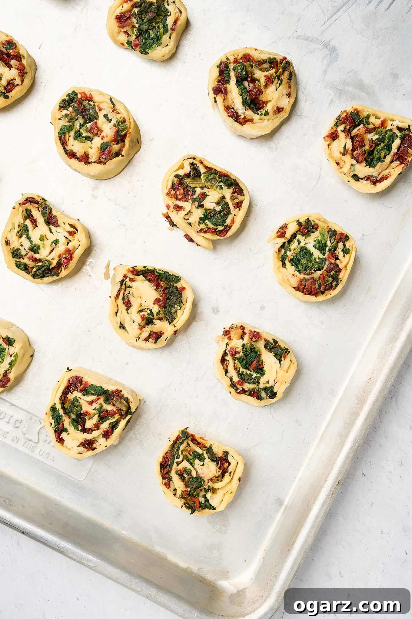 Savory Spinach Swirls 6 Sliced spinach pinwheel rounds arranged on a baking sheet, ready to bake.