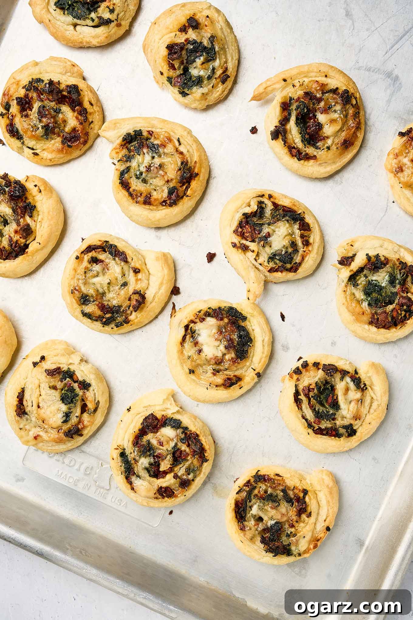 Savory Spinach Swirls 7 Golden spinach pinwheels fresh from the oven on a baking sheet, with crisp pastry and visible spinach and tomatoes.