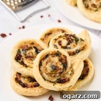 Golden spinach pinwheels made with puff pastry, spinach, sun-dried tomatoes, and cheese, stacked on a white plate.