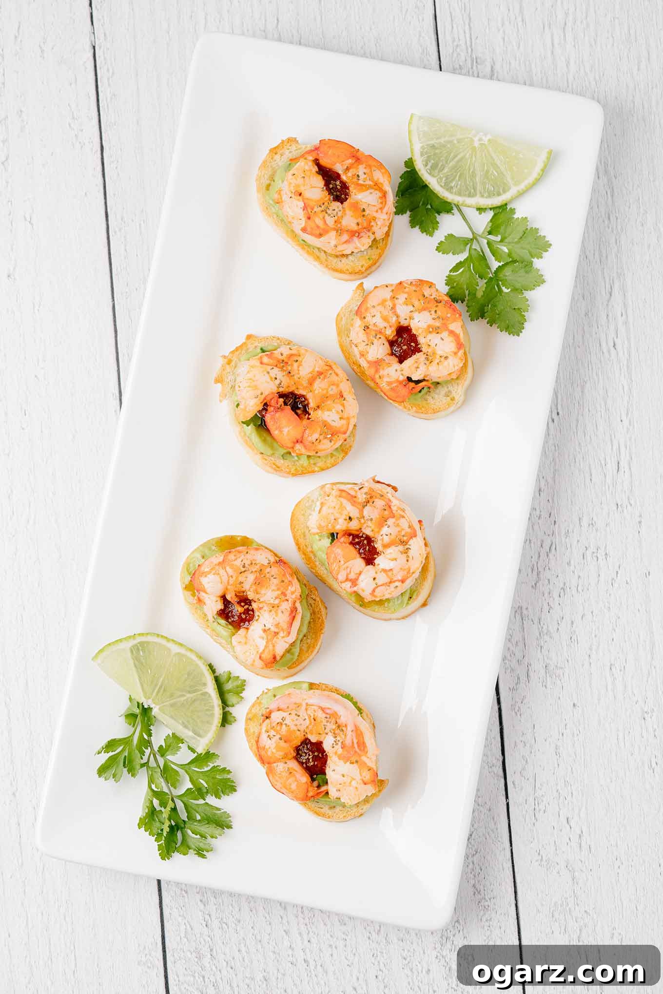 A vibrant serving platter filled with exquisite shrimp and avocado crostini, artfully garnished with fresh cilantro and bright lime wedges. An ideal gourmet appetizer for any festive occasion.