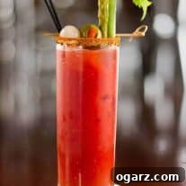 Tall glass of Bloody Mary cocktail garnished with celery stalk, pickled asparagus, green olive, and cocktail onion, served with a spiced rim and black straw.