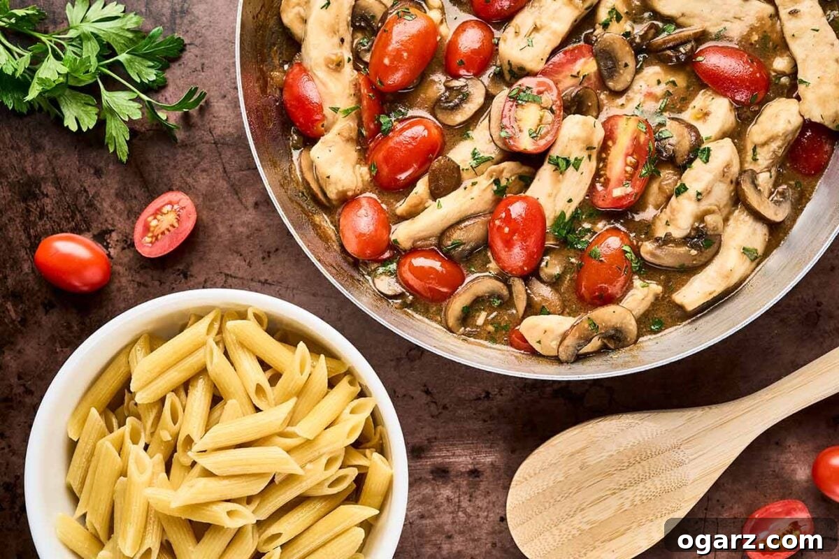 Savory Marsala Chicken and Tomato Pasta 6 A frying pan filled with chicken Marsala with fresh tomatoes next to a bowl of cooked penne pasta, ready to be combined to finish the dish.