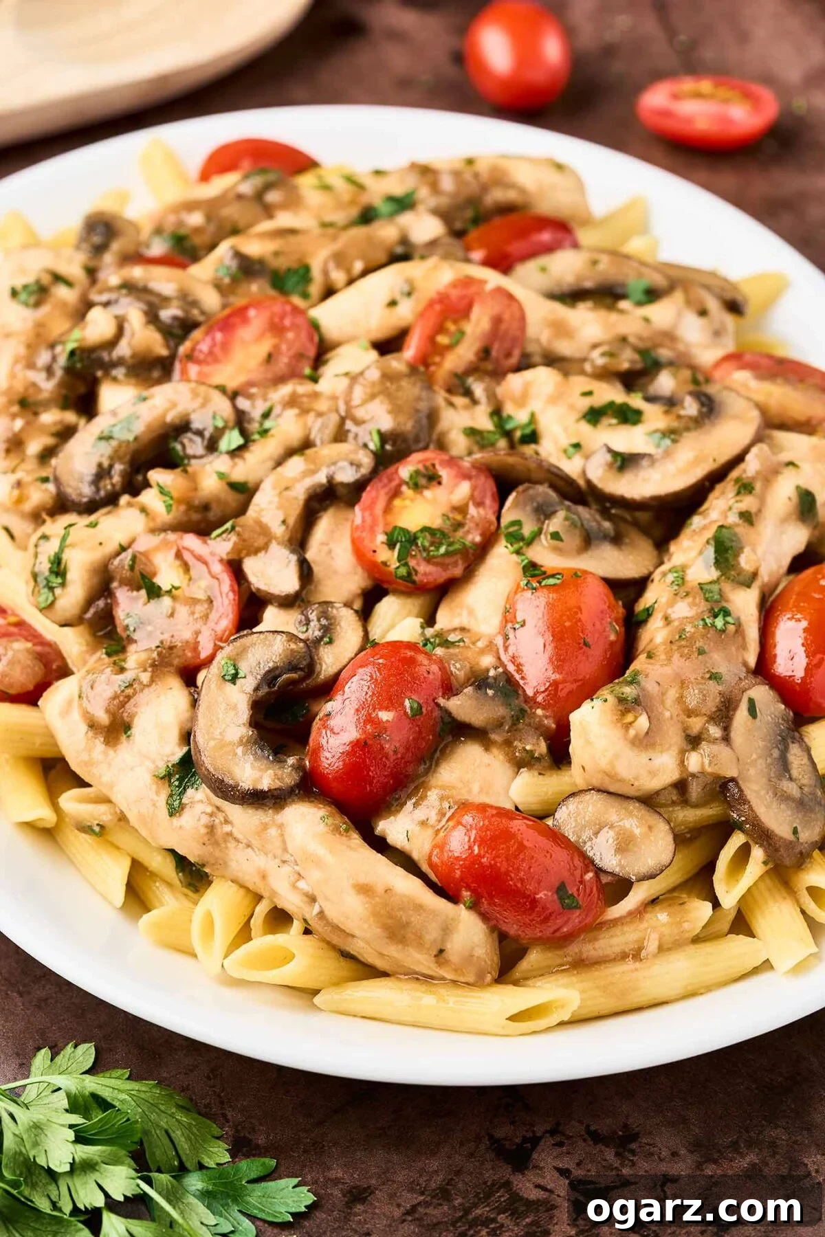 Savory Marsala Chicken and Tomato Pasta 7 A serving platter of penne pasta topped with chicken Marsala with fresh tomatoes, garnished with chopped parsley.