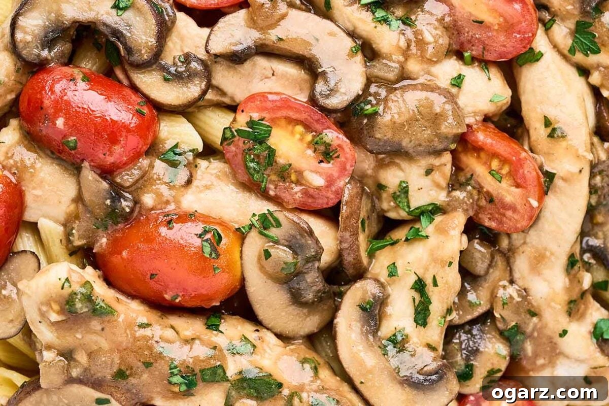 Savory Marsala Chicken and Tomato Pasta 8 A close up look at chicken Marsala pasta showing chicken breast strips, penne pasta, mushrooms, grape tomatoes, bits of garlic, and chopped parsley.