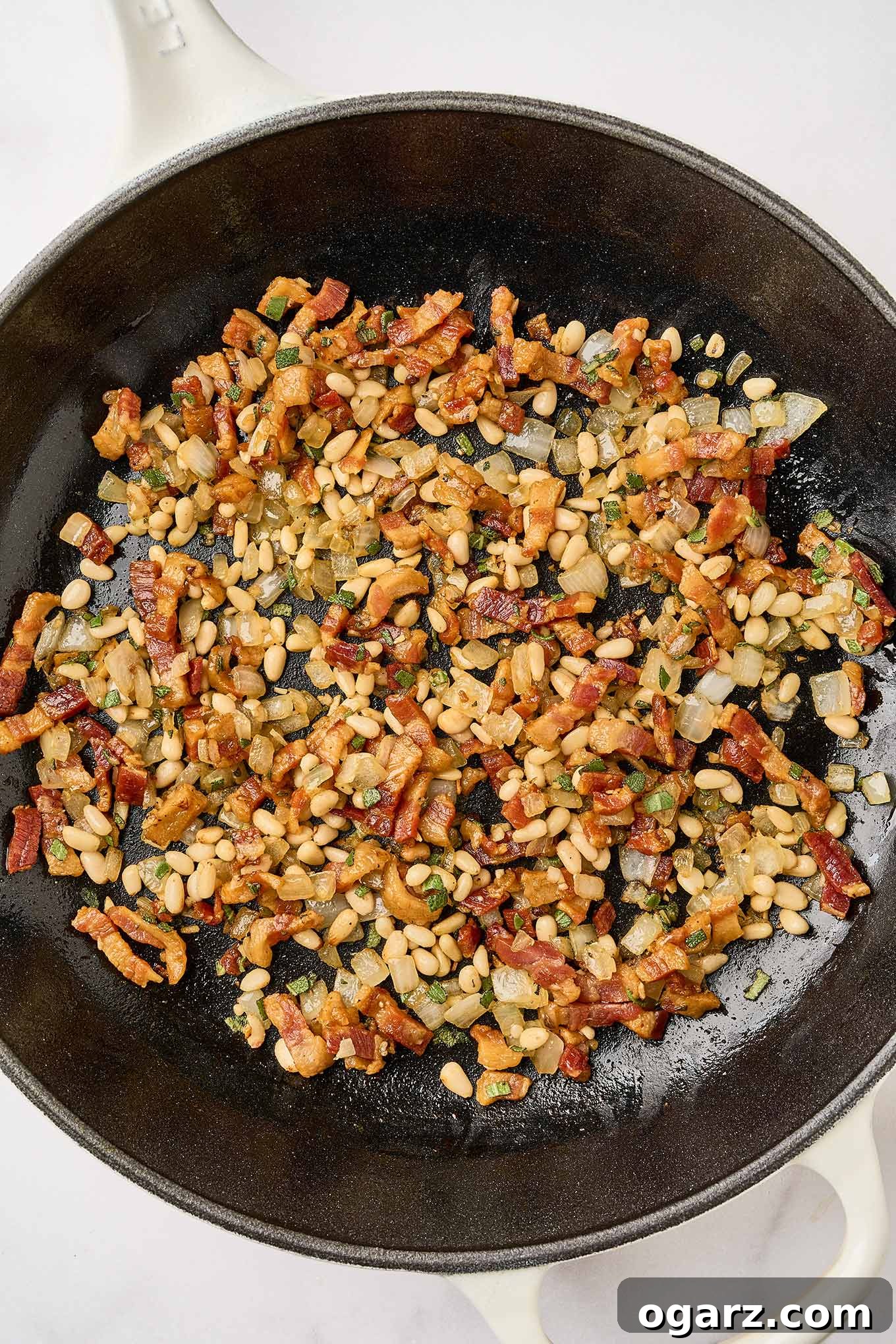 Preparing creamy pumpkin pasta, by combining fried pancetta with sautéed onions, garlic, and pine nuts in a cast iron skillet.
