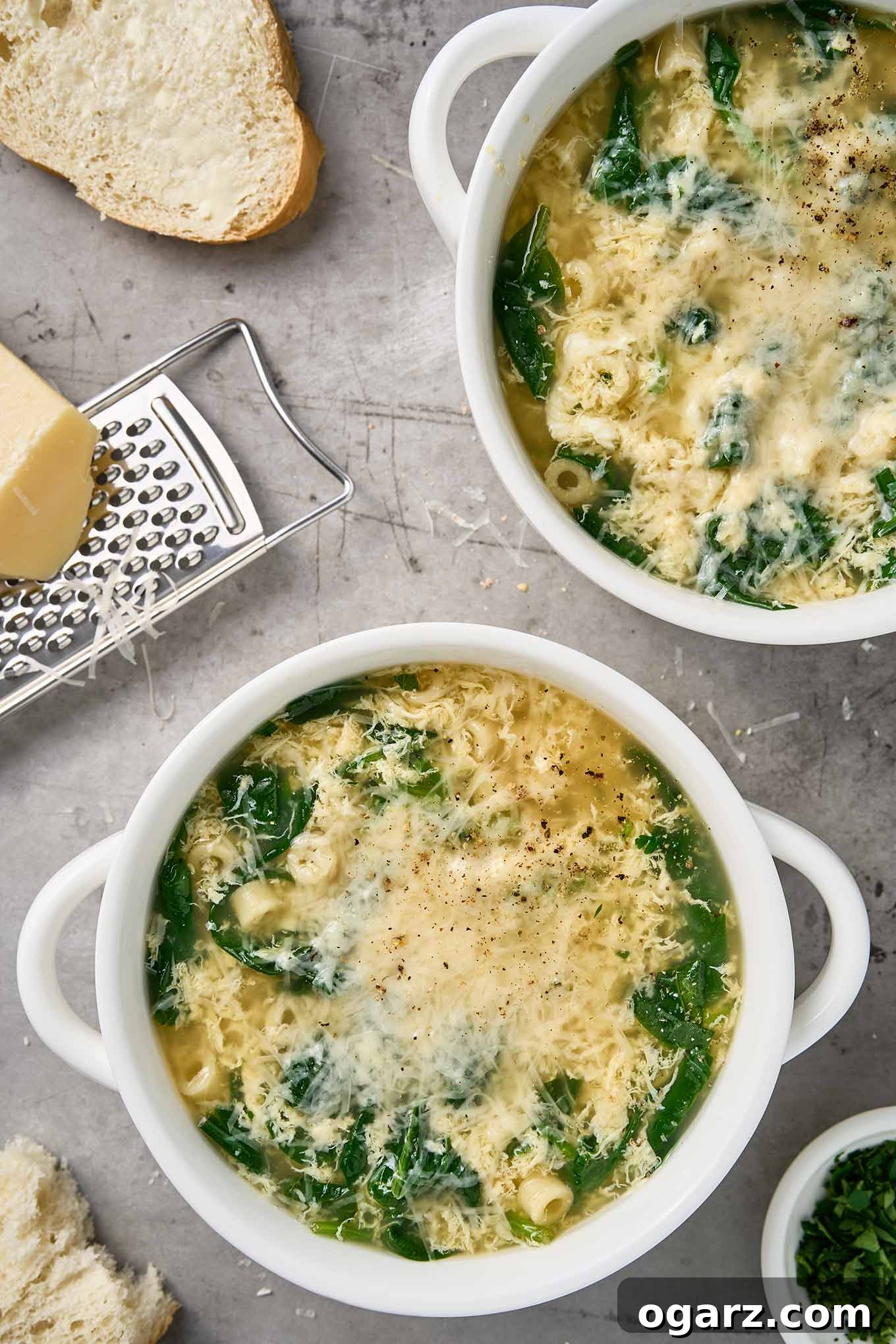 Spinach Pasta Stracciatella Soup 2 Bowls of stracciatella soup with spinach, ditalini, and grated Parmigiano-Reggiano, shown with bread and a cheese grater.
