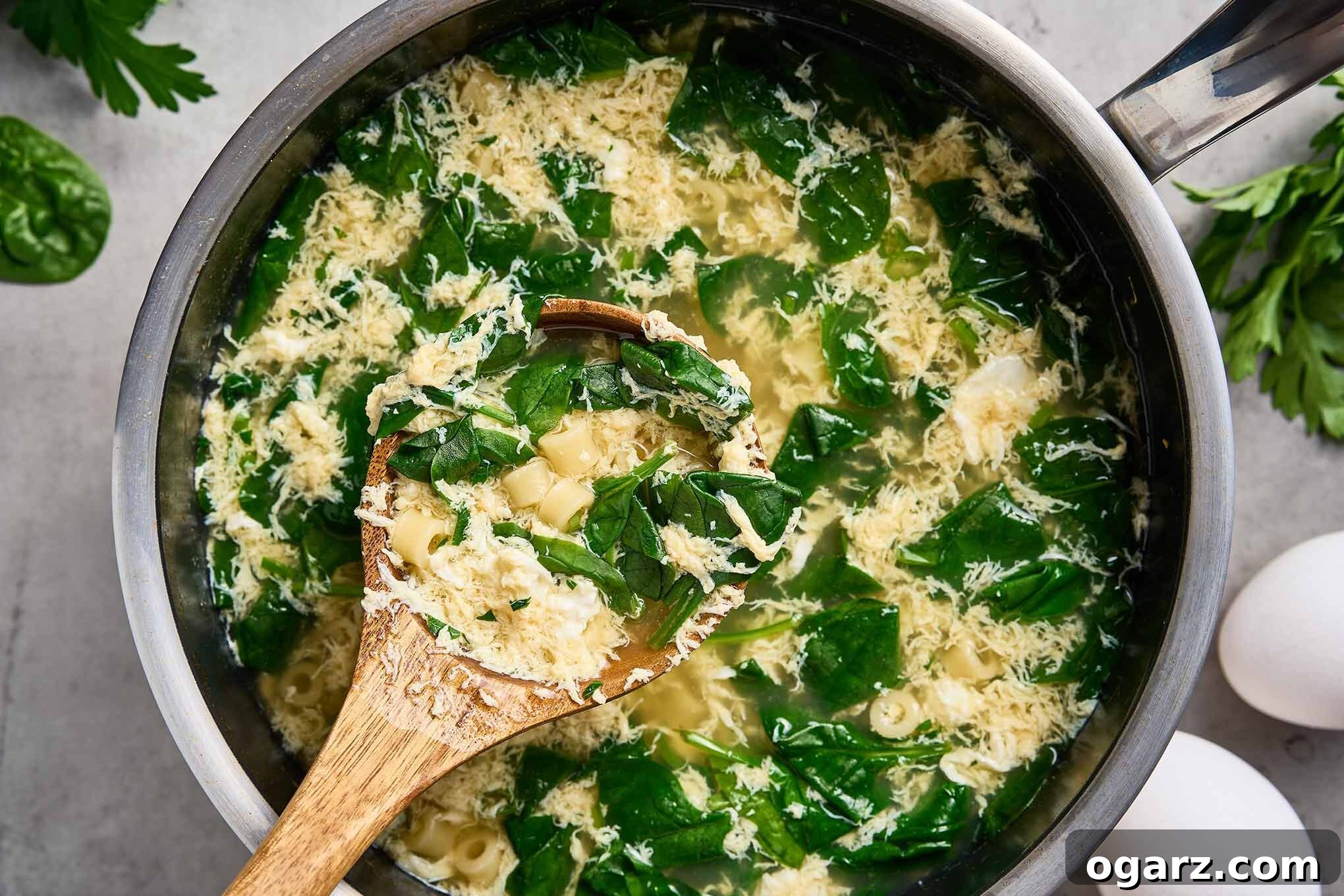 Spinach Pasta Stracciatella Soup 6 Wooden spoon showing spinach, ditalini pasta, and egg ribbons lifted from a pot of stracciatella soup.