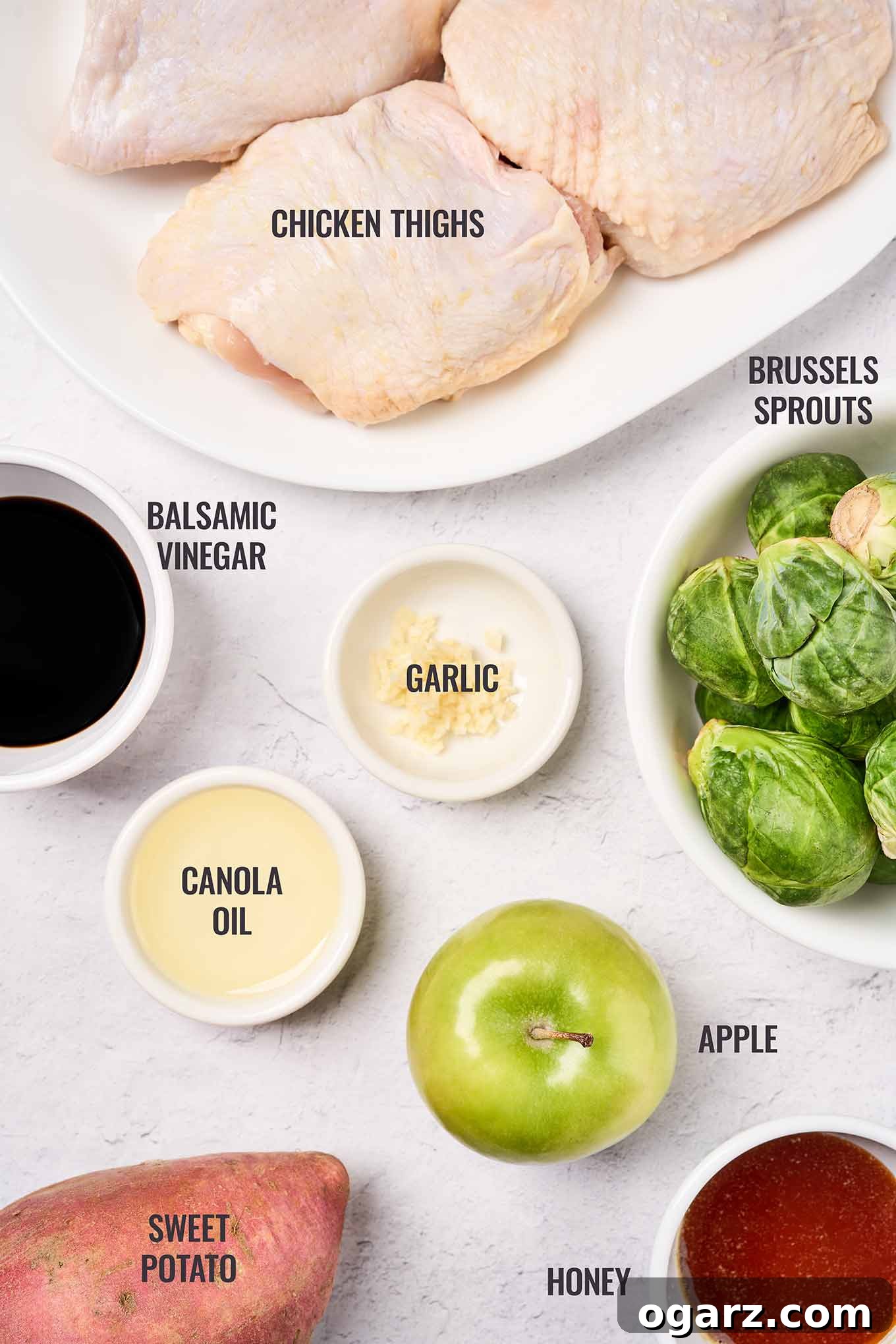 One-Pan Chicken and Seasonal Veggies 3 Labeled, overhead view of the ingredients for sheet pan chicken thighs including sweet potatoes, Brussels sprouts, apple, balsamic vinegar, and honey. All ingredients are neatly arranged for easy viewing.