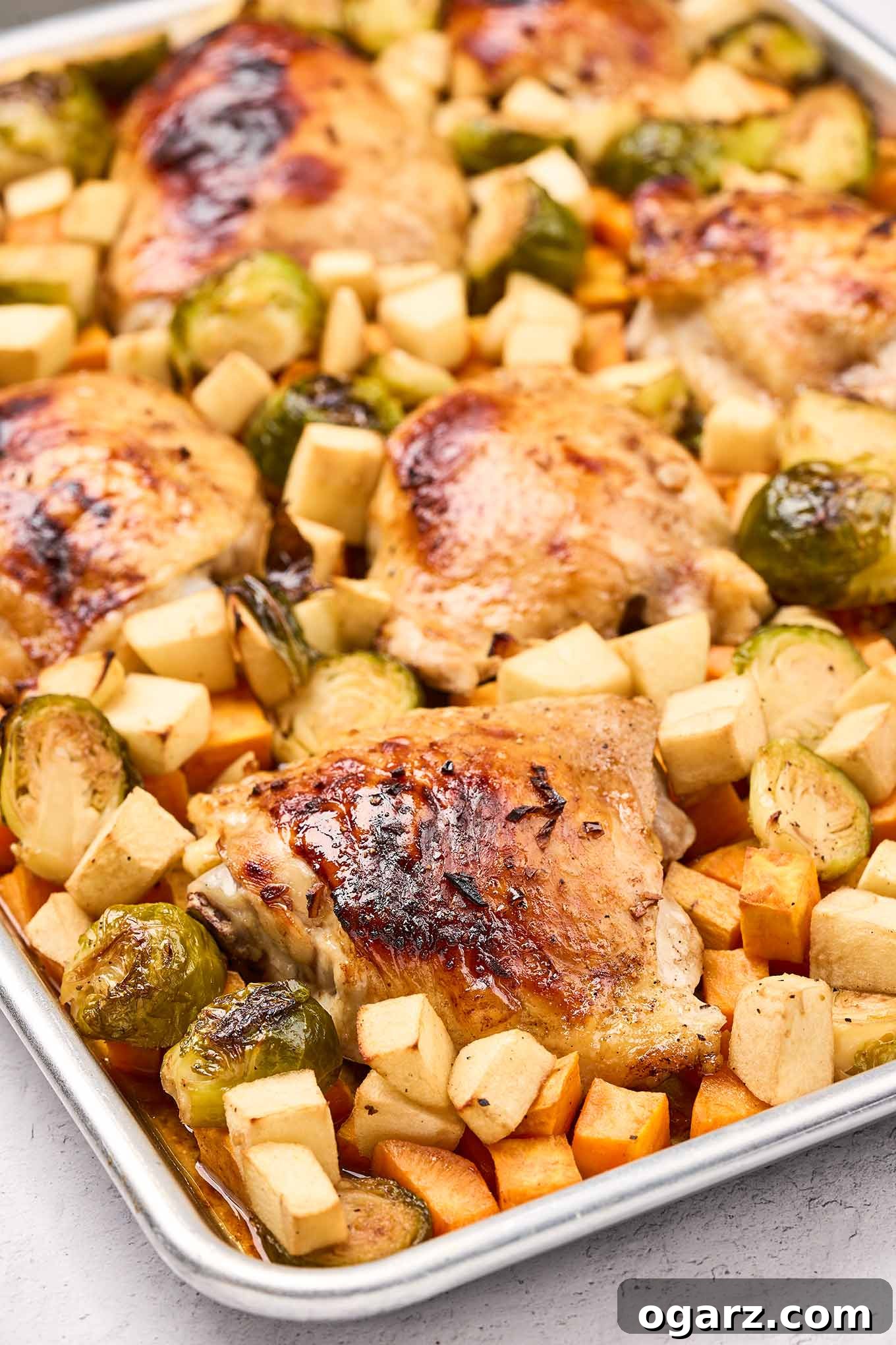 One-Pan Chicken and Seasonal Veggies 4 A sheet pan filled with roasted chicken thighs, Brussels sprouts, apples, and sweet potatoes, fresh out of the oven, ready to be served.