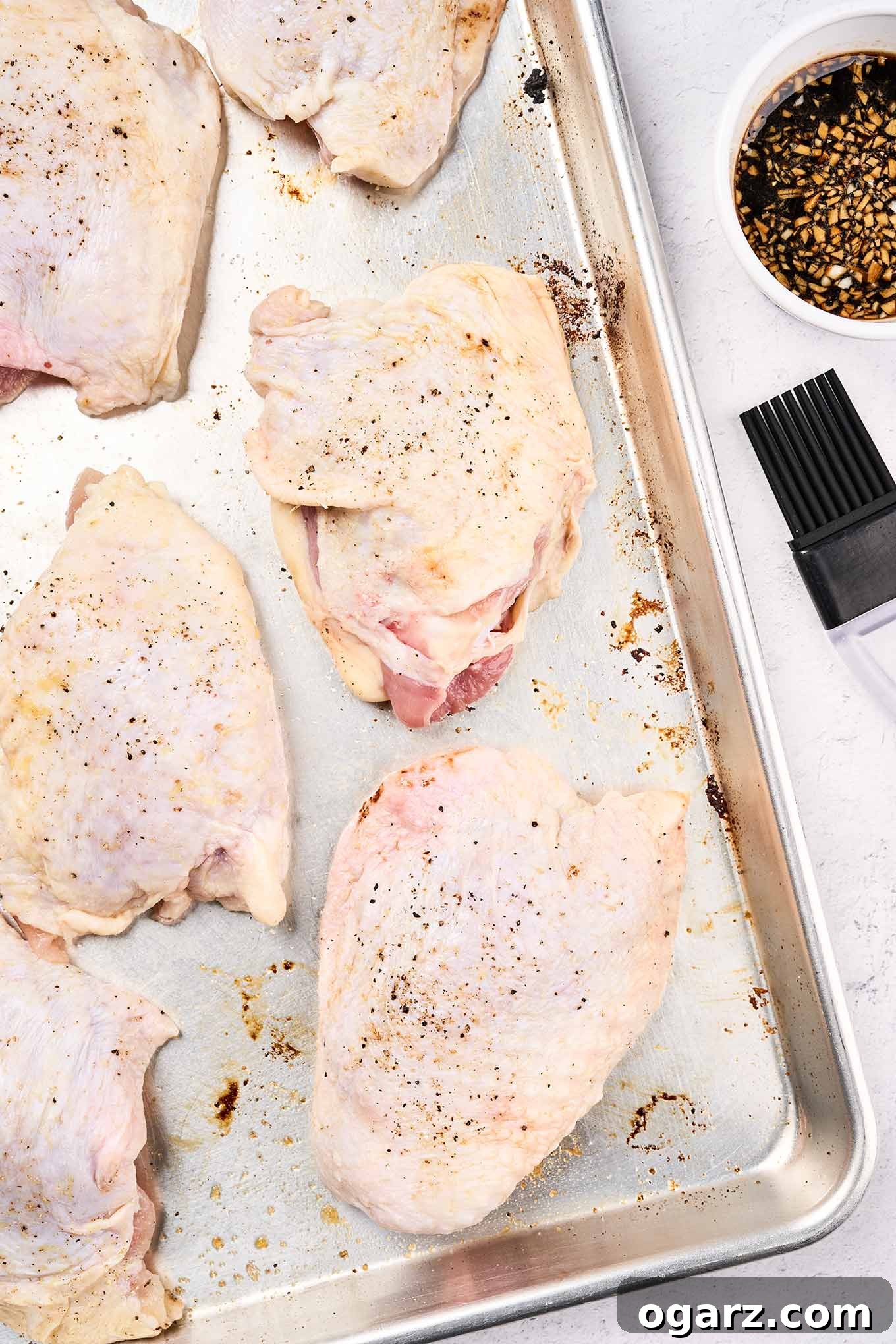 One-Pan Chicken and Seasonal Veggies 6 Bone-in chicken thighs arranged on a sheet pan, seasoned and ready for the oven. The chicken is positioned centrally on the pan.