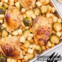 An overhead view of sheet pan chicken with seasonal vegetables next to black serving utensils and a glass of white wine.