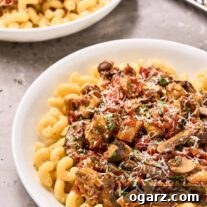 Two bowls of eggplant and mushroom tomato ragu over cavatappi pasta, a sprinkling of finely grated Parmesan cheese and chopped parsley on top, metal grater in the background.