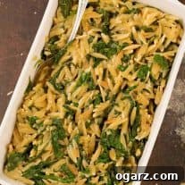 An overhead view of a casserole of toasted orzo and sautéed spinach side dish, with a serving spoon.