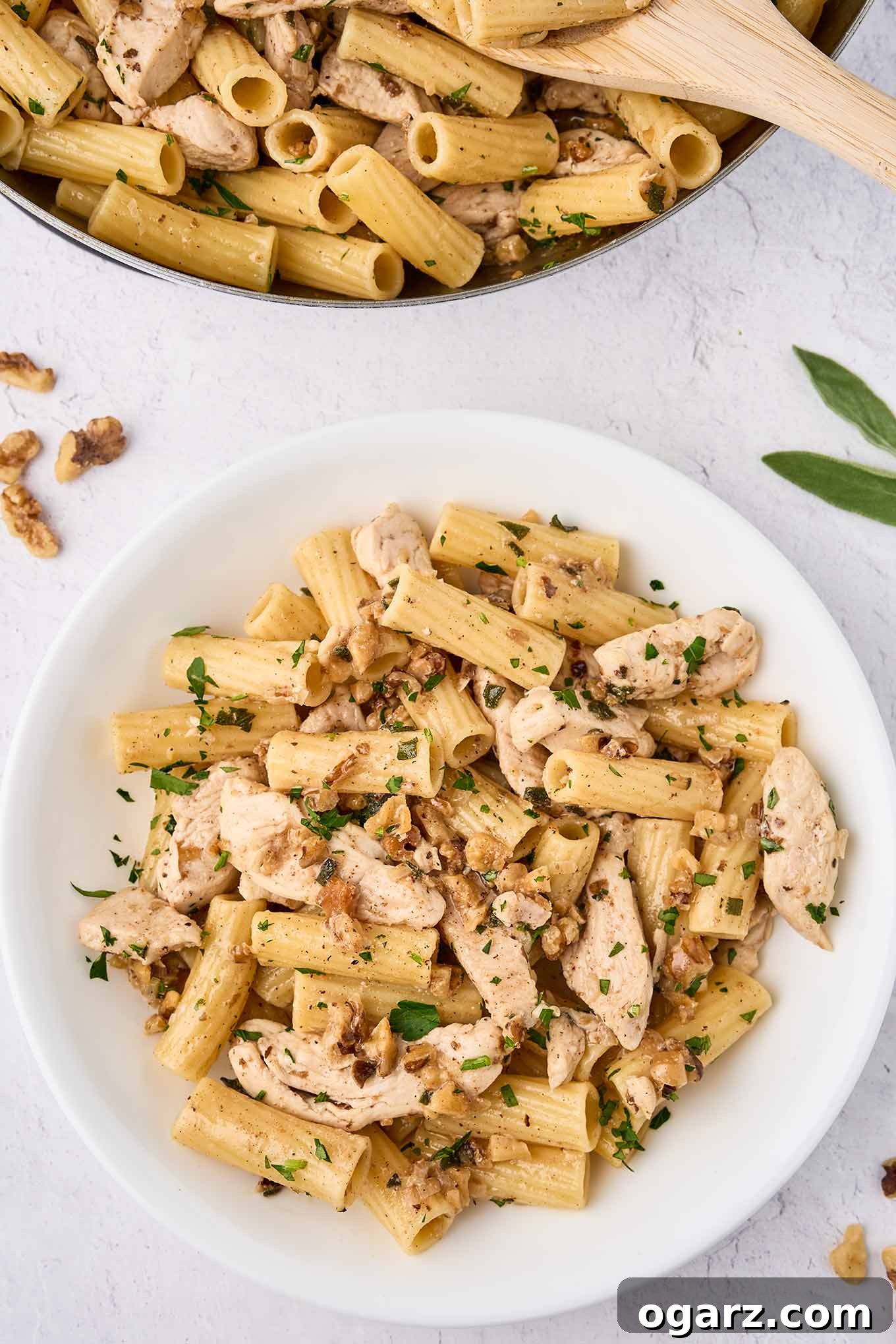 Nutty Brown Butter Chicken Pasta 2 An overhead view of brown butter chicken pasta being spooned into a serving bowl from the skillet. Golden pasta strands, tender chicken, and vibrant sage leaves are visible.