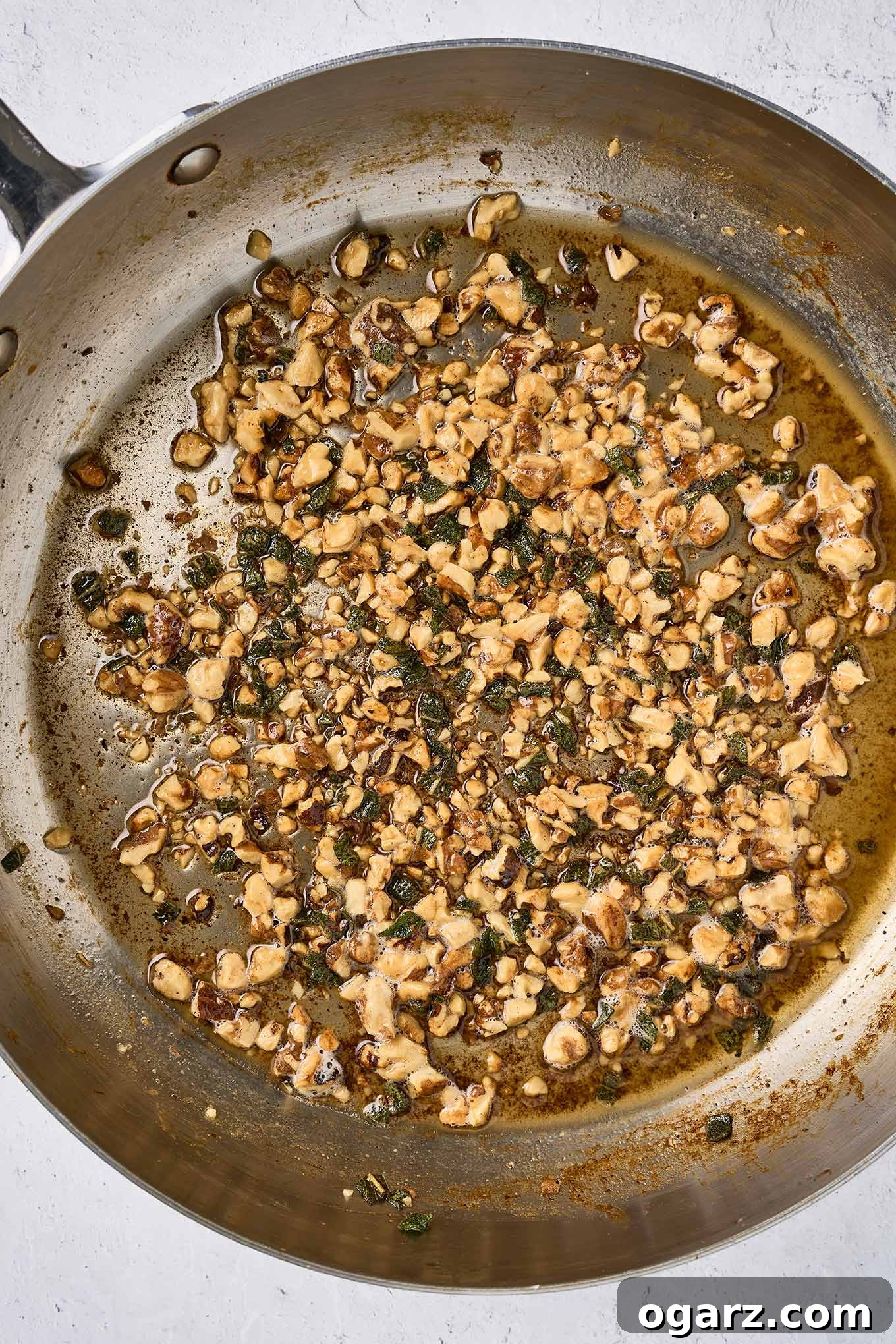Nutty Brown Butter Chicken Pasta 6 The second step in preparing brown butter chicken pasta - sautéing chopped walnuts and fresh sage in brown butter. Perfectly browned milk solids are visible at the bottom of the pan, indicating a rich, nutty flavor.