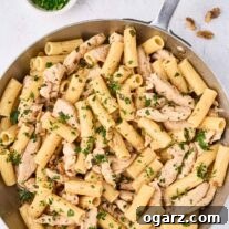 An overhead view of a skillet filled with brown butter pasta and tender strips of chicken, garnished with parsley - a prep bowl with more chopped parsley to the side.