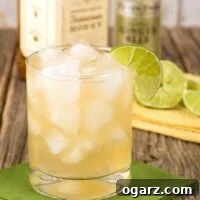 A rocks glass filled with a cocktail of Jack Daniel's Tennessee Honey Whiskey combined with ginger beer and garnished with lime, bottles and sliced lime in the background.