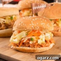 A cutting board with four pulled bbq pulled chicken sliders topped with homemade slaw and served on sesame seed buns.