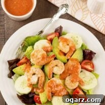Overhead view of a salad of mixed greens, cucumber slices, avocado, tomatoes, and shrimp, topped with cocktail sauce dressing.