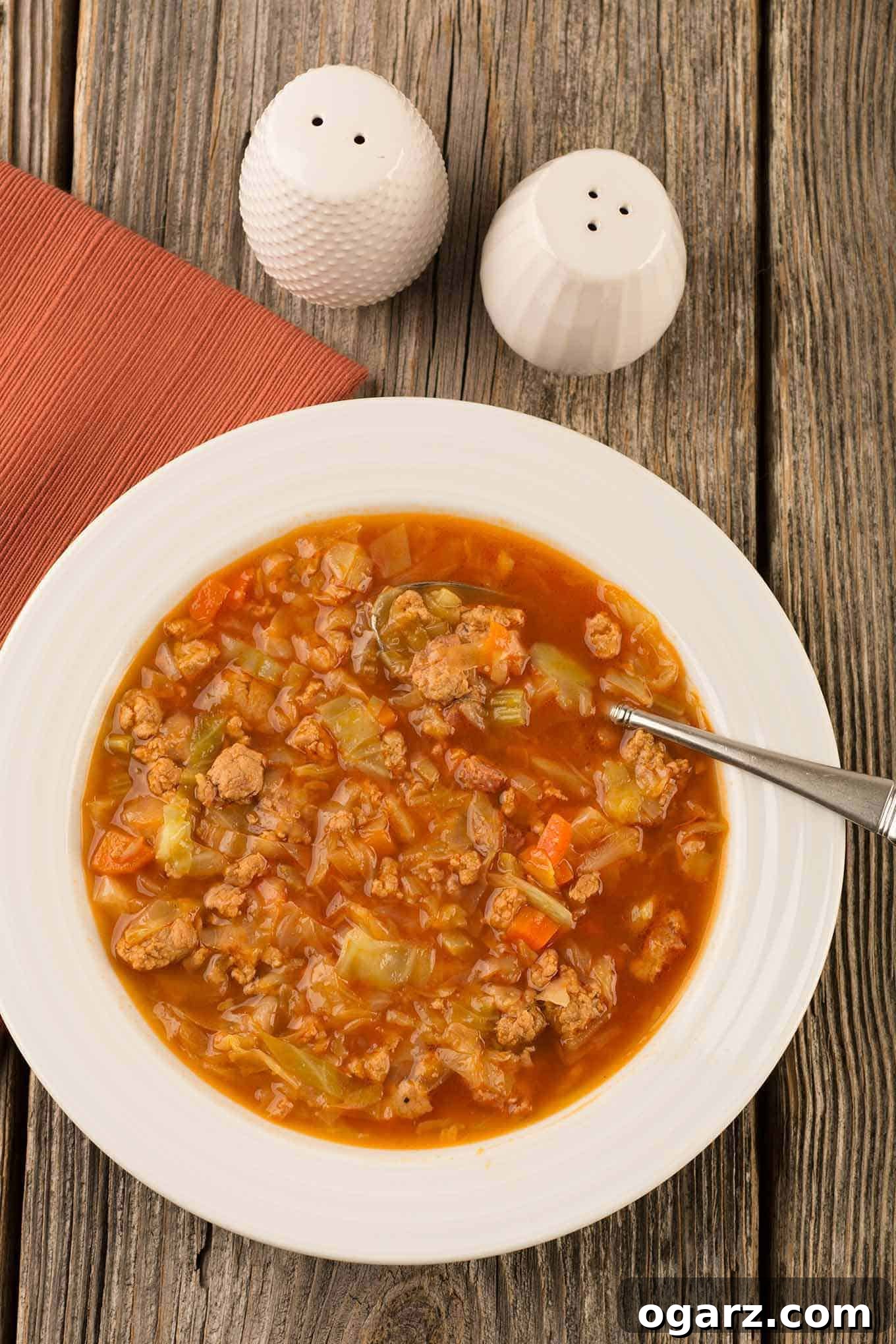 Quick & Cozy Cabbage Soup 2 An overhead view of Instant Pot cabbage, ground turkey and smoked sausage soup in a bowl with a spoon on a rustic wooden surface. A perfect hearty, low-carb meal.