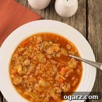 An overhead view of Instant Pot cabbage, ground turkey and smoked sausage soup in a bowl with a spoon on a rustic wooden surface.
