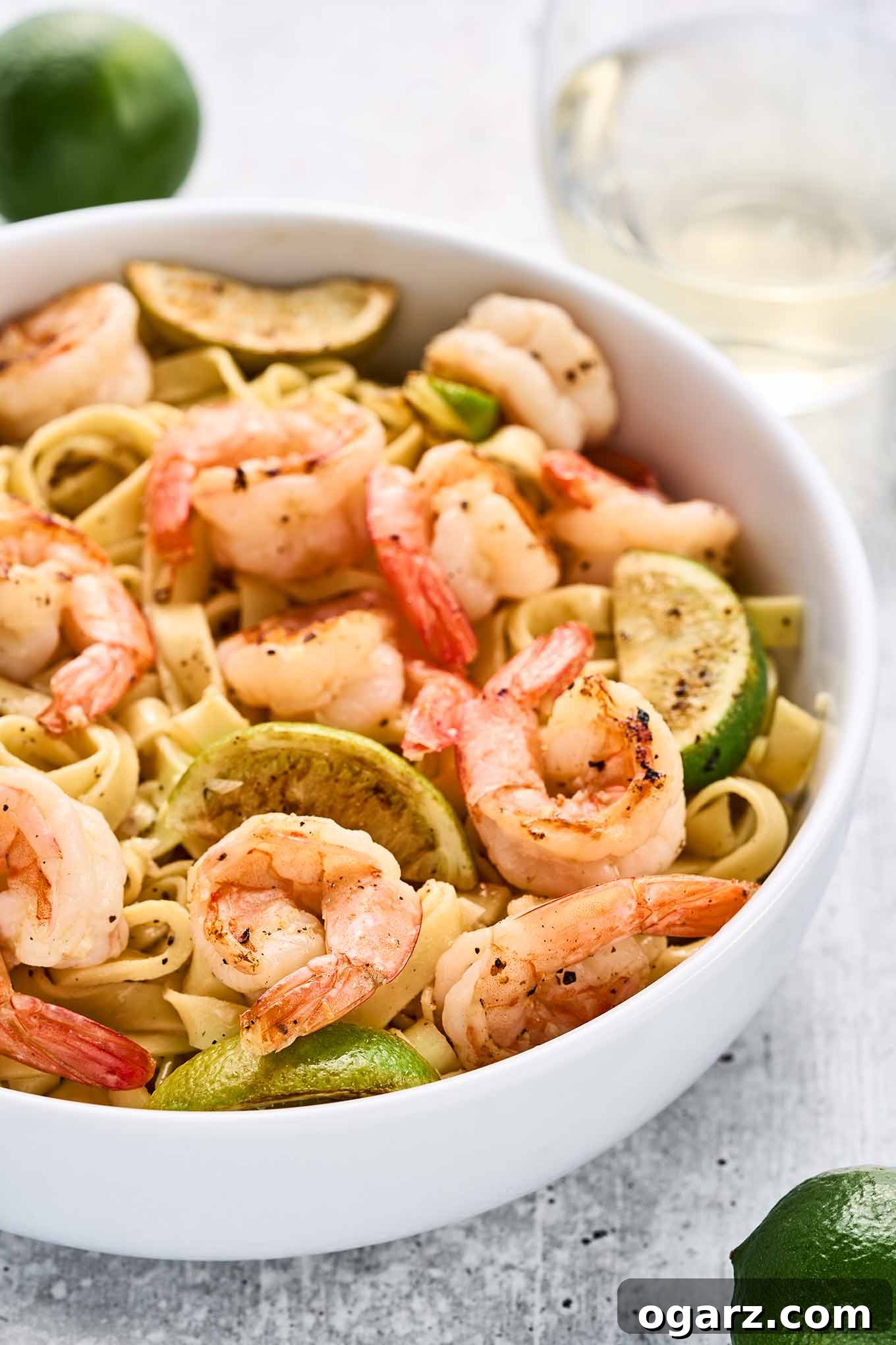 Zesty Garlic Lime Shrimp Pasta 5 Close view of garlic lime shrimp tossed with fettuccine, showcasing the plump shrimp, pan-seared lime wedges, and tender pasta in a white bowl.