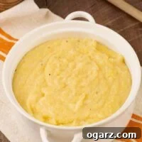 A round, white casserole of creamy polenta atop a striped tea towel with a wooden spoon to the rear.
