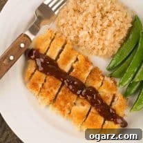 An overhead view a plate with Japanese breaded pork cutlet, sliced and topped with a drizzle of katsu sauce, served with riced cauliflower and sautéed snap peas.