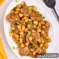An oval serving platter of Caribbean-style pineapple pork with tender pork medallions, pineapple chunks, and scallions in a sweet-savory rum sauce.