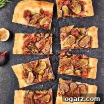 Slices of fig and prosciutto pizza on a slate background surrounded by fresh figs and sprigs of rosemary.