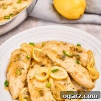 A shallow white serving bowl filled with lemon pepper chicken tenders in pan sauce, garnished with lemon slices and chopped scallions