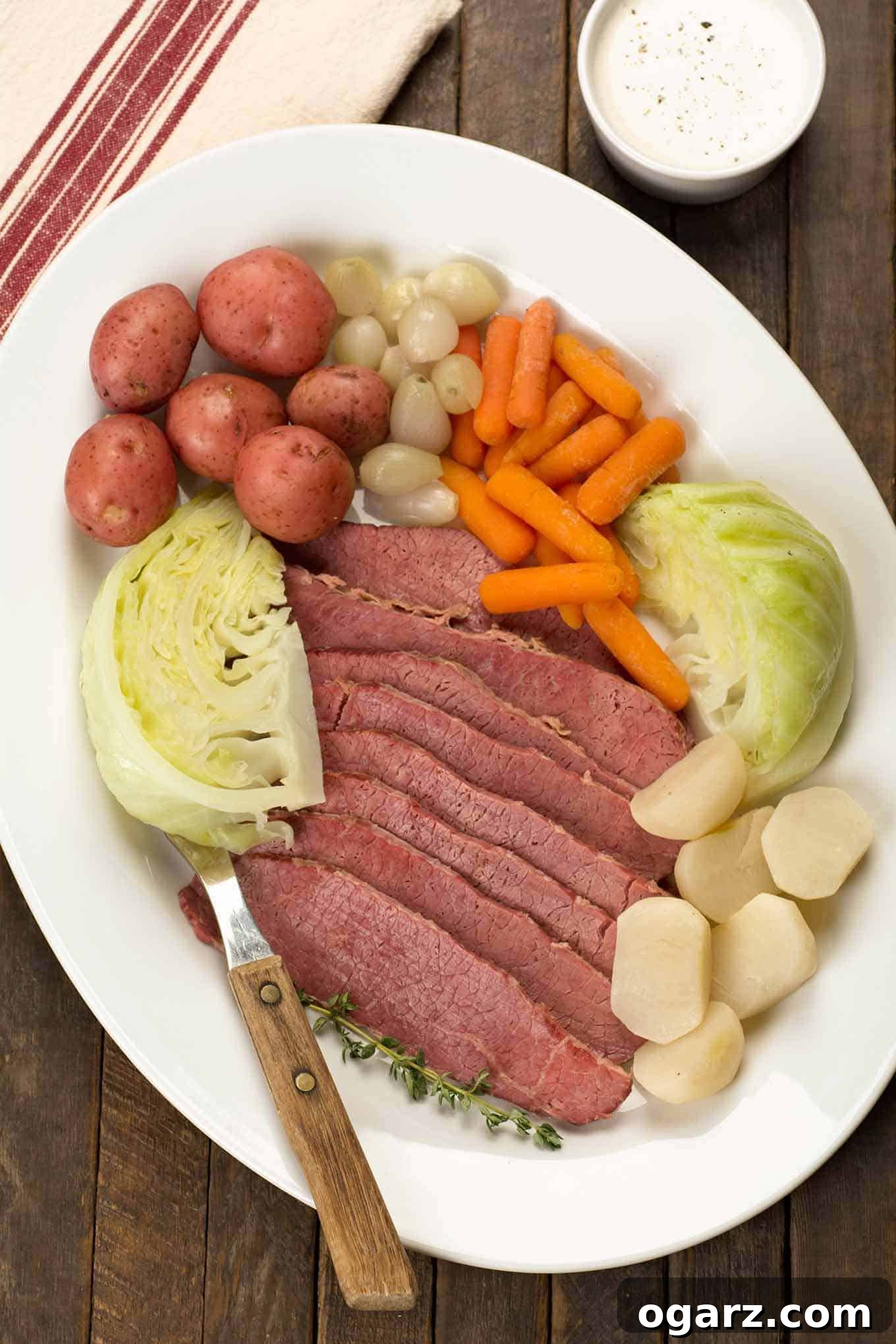 A hearty serving platter featuring traditional New England Boiled Dinner: perfectly sliced corned beef brisket, tender cabbage wedges, small red potatoes, sweet baby carrots, delicate pearl onions, and savory turnips, ready to be enjoyed.