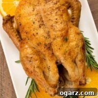A whole roasted duck with crisp, golden brown skin on a serving platter garnished with orange slices and sprigs of fresh rosemary.