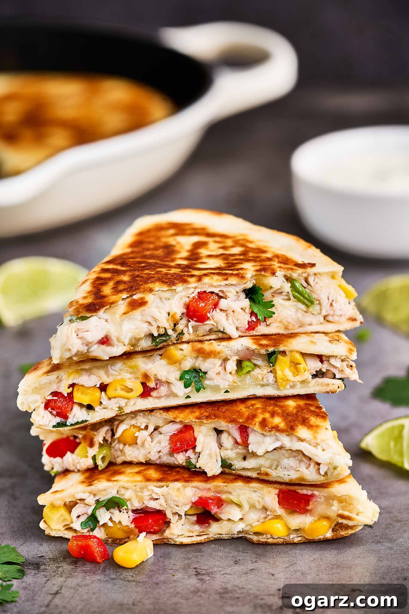 Ultimate Chicken and Cheese Quesadillas 2 Golden brown chicken and cheese quesadillas, expertly cut into wedges and neatly stacked on a rustic wooden board, accompanied by vibrant lime wedges, fresh cilantro sprigs, and a creamy dish of homemade sour cream dip.