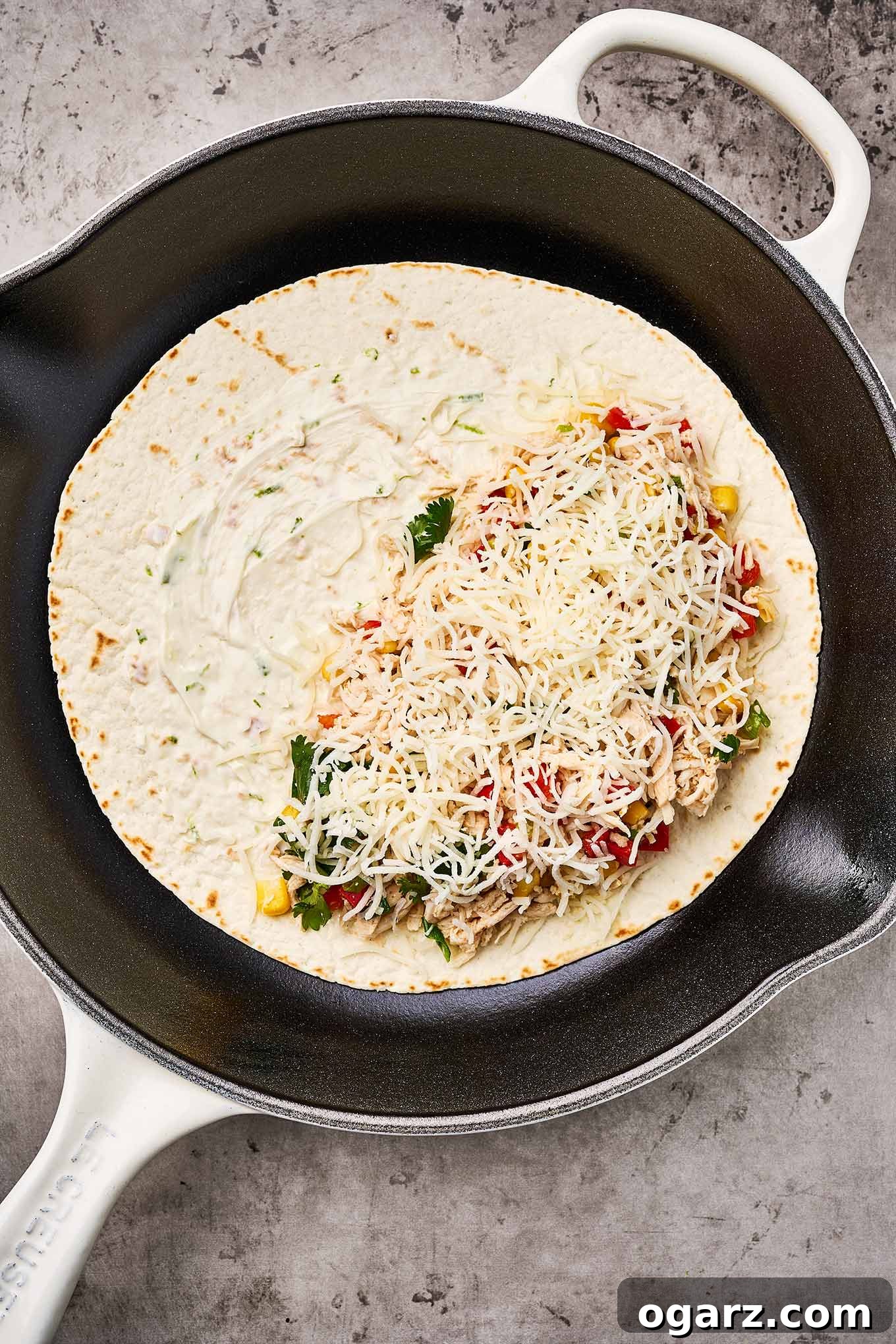 Ultimate Chicken and Cheese Quesadillas 4 A step-by-step photo demonstrating how to expertly add the chicken and cheese filling to one half of a tortilla, positioned in a skillet, ensuring easy folding and turning during the cooking process.