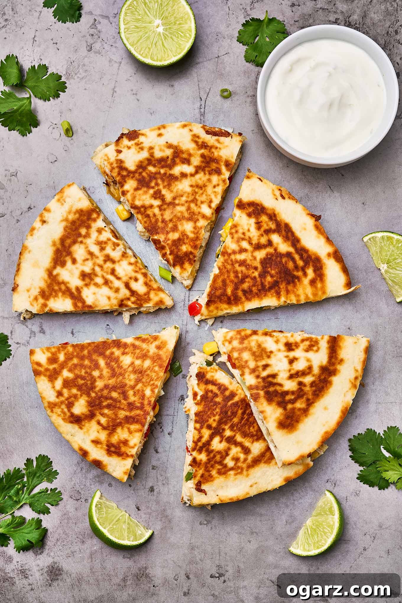 Ultimate Chicken and Cheese Quesadillas 5 An inviting overhead view of perfectly cooked chicken and cheese quesadillas, meticulously sliced into neat wedges and arranged around vibrant lime slices, fresh sprigs of cilantro, and a small bowl of creamy sour cream, ready for dipping.