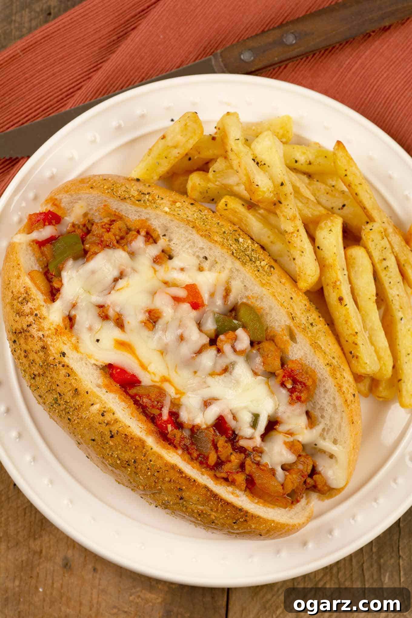 Zesty Italian Handhelds 2 A plate with a sub roll filled with a sloppy-Joe style mix of crumbled Italian sausage, green pepper, tomato sauce, and melted mozzarella, fries on the side. The sandwich is generously filled, showcasing the vibrant colors of the peppers and sauce, with rich, melted cheese creating an inviting, indulgent appearance. Golden fries are perfectly crisp beside the main dish.