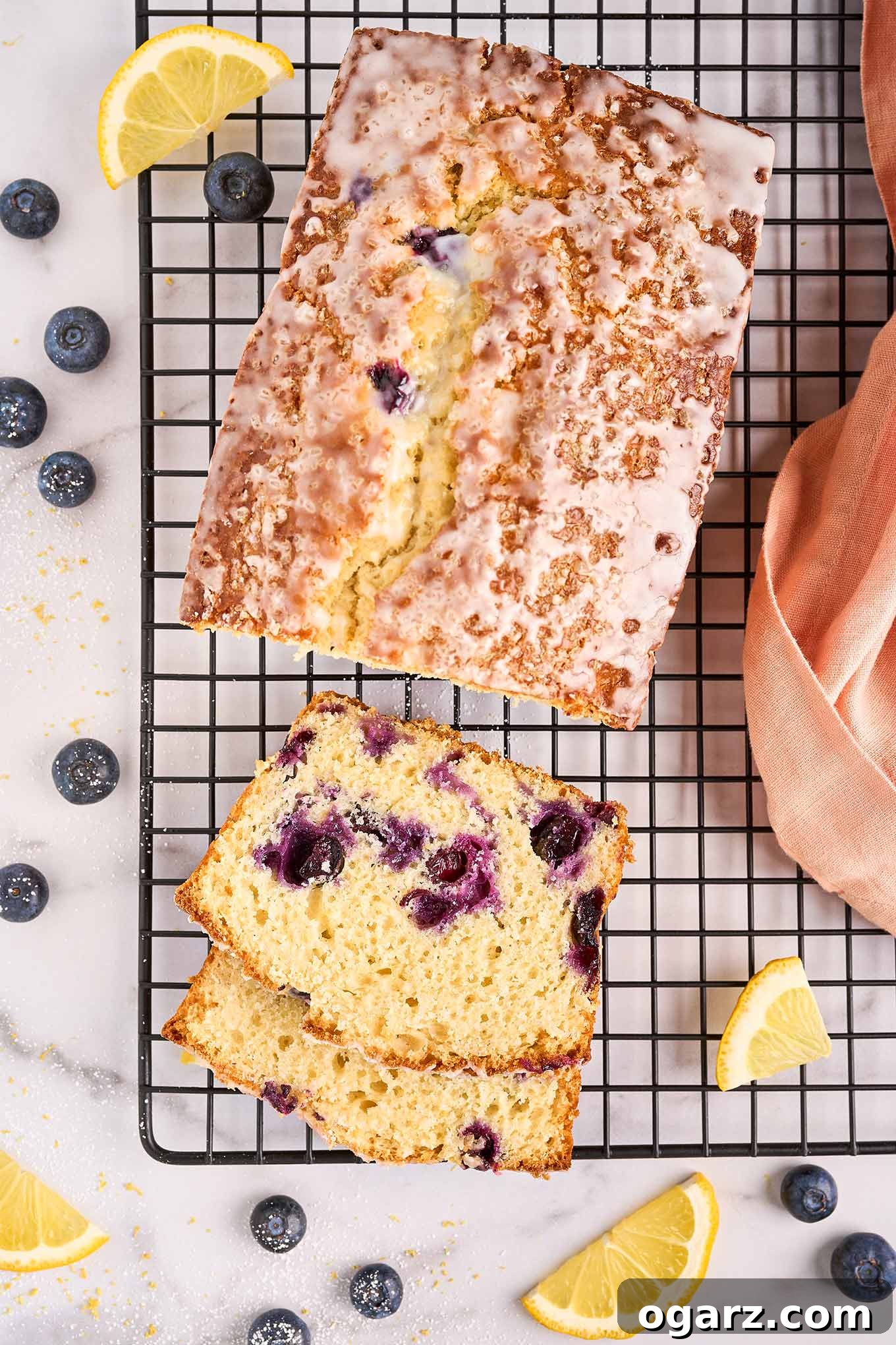 Sunshine Lemon Blueberry Loaf 2 Freshly baked lemon blueberry loaf cake on a black wire rack. Slices reveal moist crumb studded with plump blueberries, drizzled with a sweet lemon glaze. It's a perfect summer dessert.