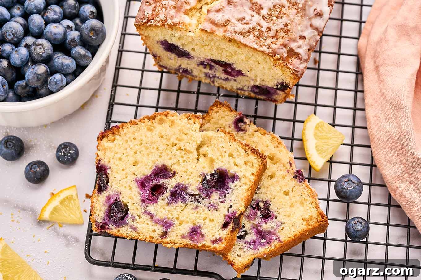 Sunshine Lemon Blueberry Loaf 5 Close-up of a sliced lemon blueberry loaf cake on a cooling rack showing juicy blueberries throughout the moist crumb, highlighting its delicious texture.