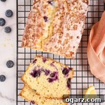 Freshly baked lemon blueberry loaf cake on a black wire rack. Slices reveal moist crumb studded with plump blueberries, drizzled with a sweet lemon glaze.